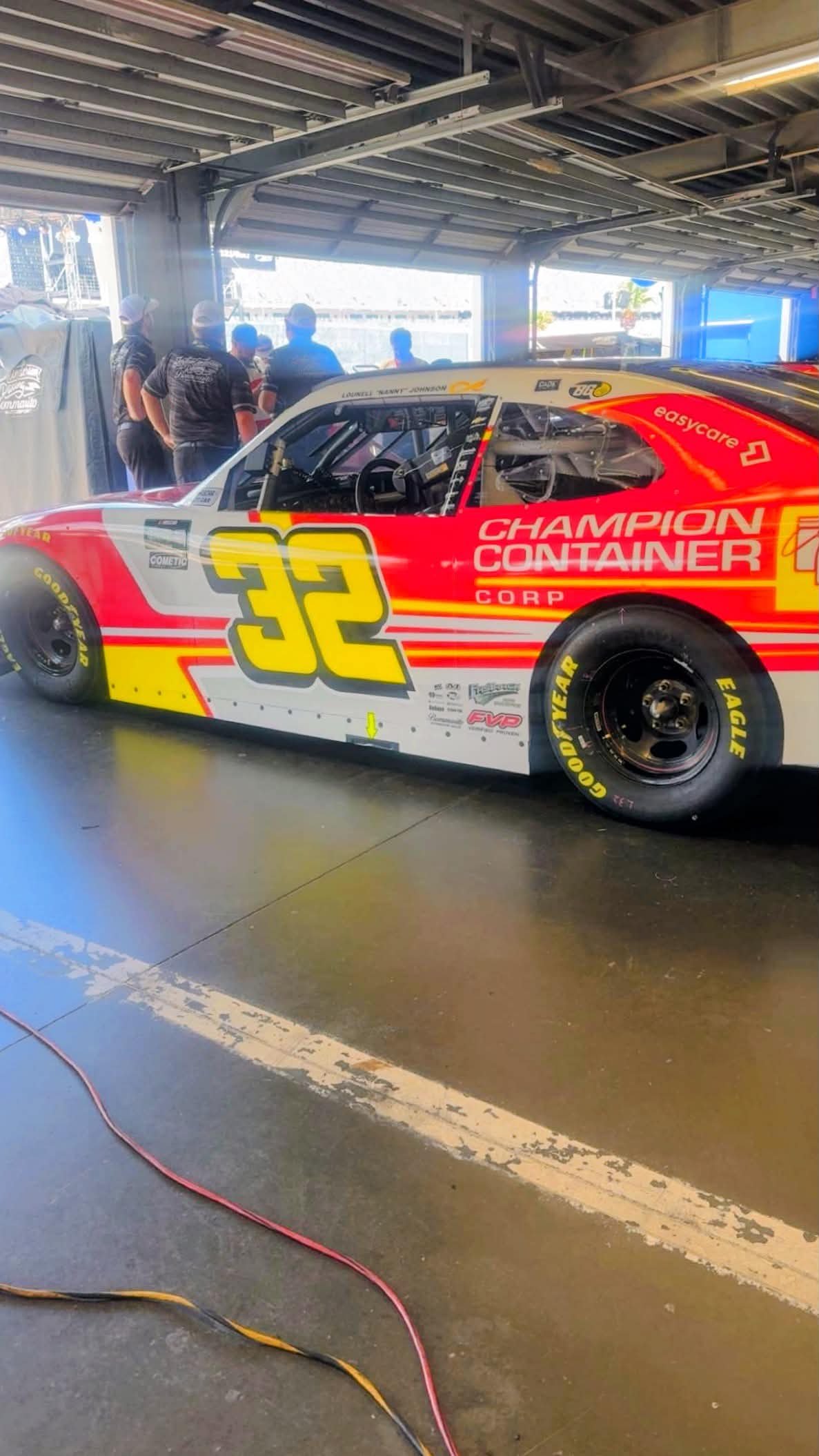 Red number 32 stock car with sponsor graphics in a garage